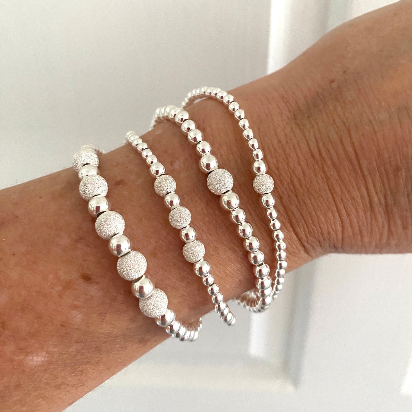 Silver stardust sparkle beaded bracelets on a wrist against a neutral background