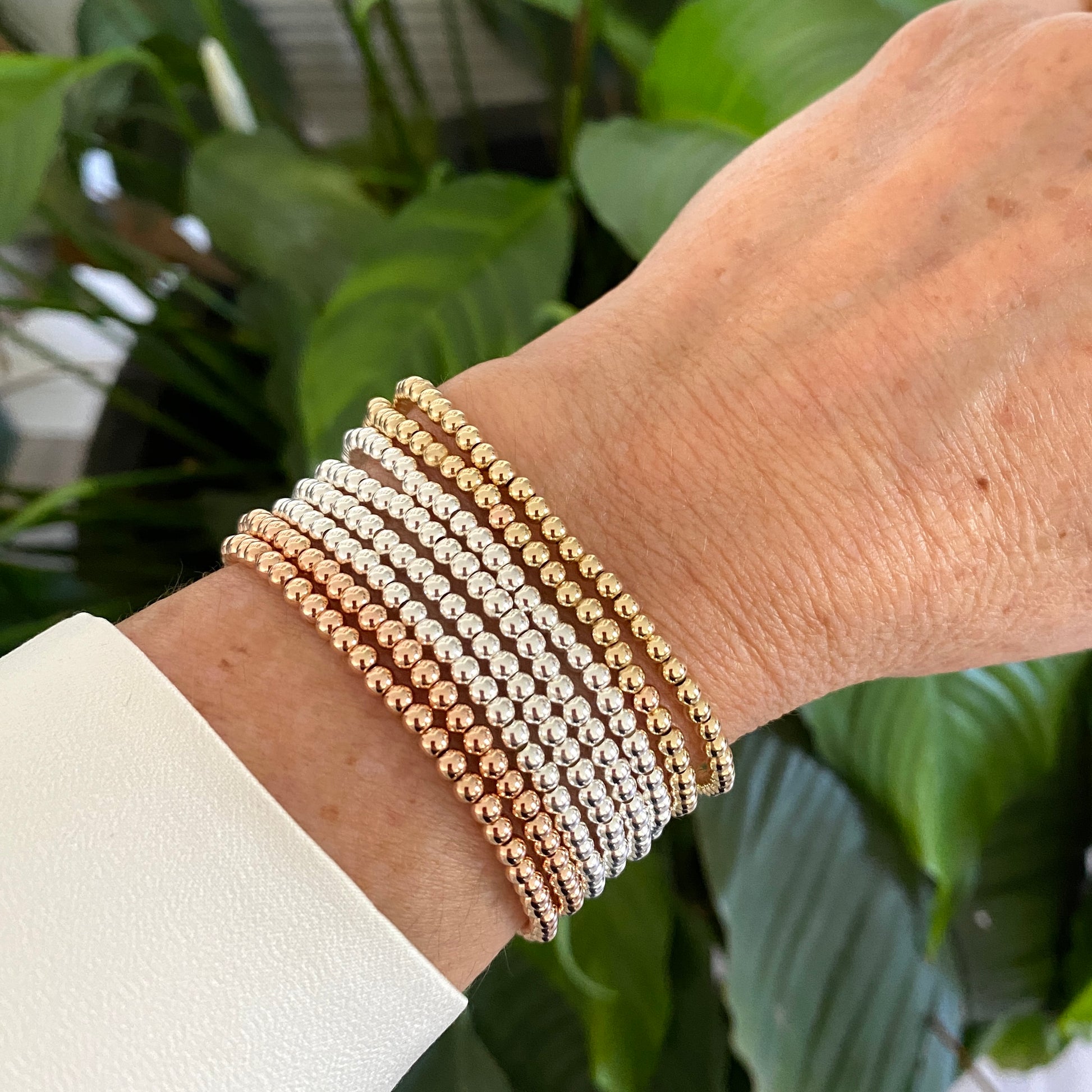 Close-up of a wrist wearing multiple beaded bracelets with a green leafy background